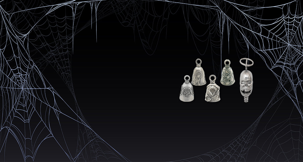 Four silver-toned Halloween-themed charms, including a skull, a halo, and three bells with gothic engravings, displayed against a dark background with white spiderwebs.